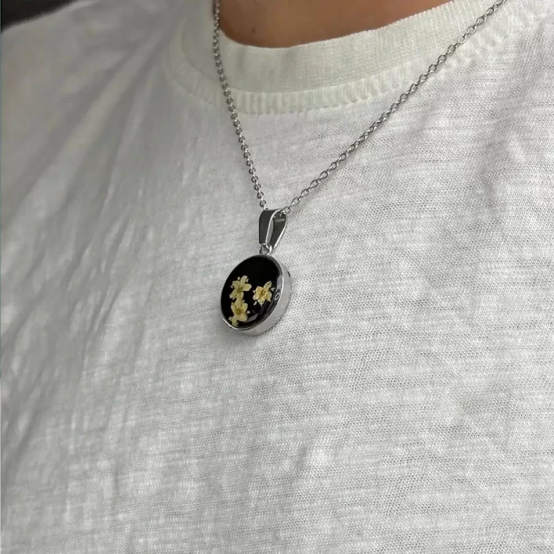 Geperste bloemen ketting met gele bloemen in rond hars medaillon aan zilverkleurige ketting op witte achtergrond