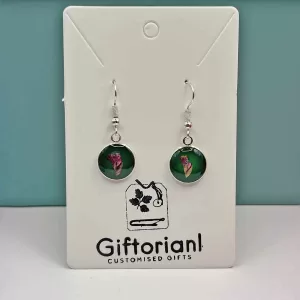 Zilverkleurige ronde oorbellen met roze bloem op groene achtergrond.