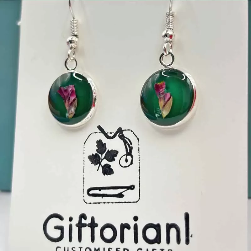 Zilverkleurige ronde oorbellen met roze bloem op groene achtergrond.