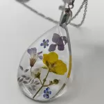 Druppelvormige geperste bloemen ketting met paarse, gele en witte echte bloemen in heldere hars aan zilverkleurige ketting