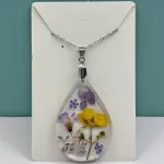 Druppelvormige geperste bloemen ketting met paarse, gele en witte echte bloemen in heldere hars aan zilverkleurige ketting