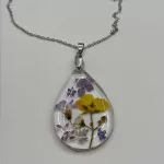 Druppelvormige geperste bloemen ketting met paarse, gele en witte echte bloemen in heldere hars aan zilverkleurige ketting
