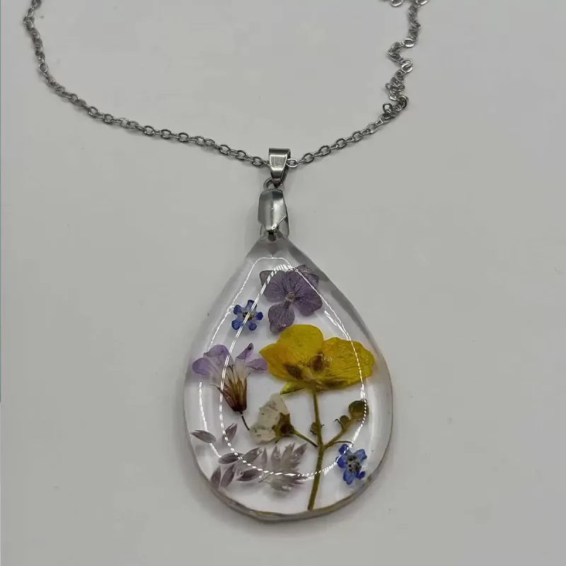Druppelvormige geperste bloemen ketting met paarse, gele en witte echte bloemen in heldere hars aan zilverkleurige ketting