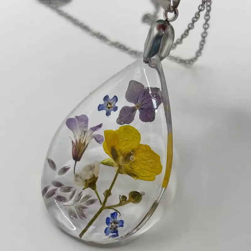 Druppelvormige geperste bloemen ketting met paarse, gele en witte echte bloemen in heldere hars aan zilverkleurige ketting