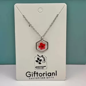 Zilverkleurige hexagon hanger met een helderrode geperste bloem.