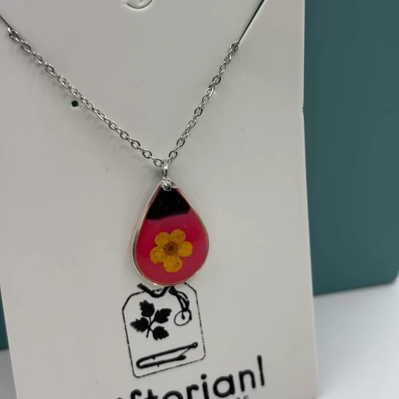 Stalen ketting met gele bloem op roze achtergrond Zilverkleurige druppelvormige hanger met gele bloem in roze hars.