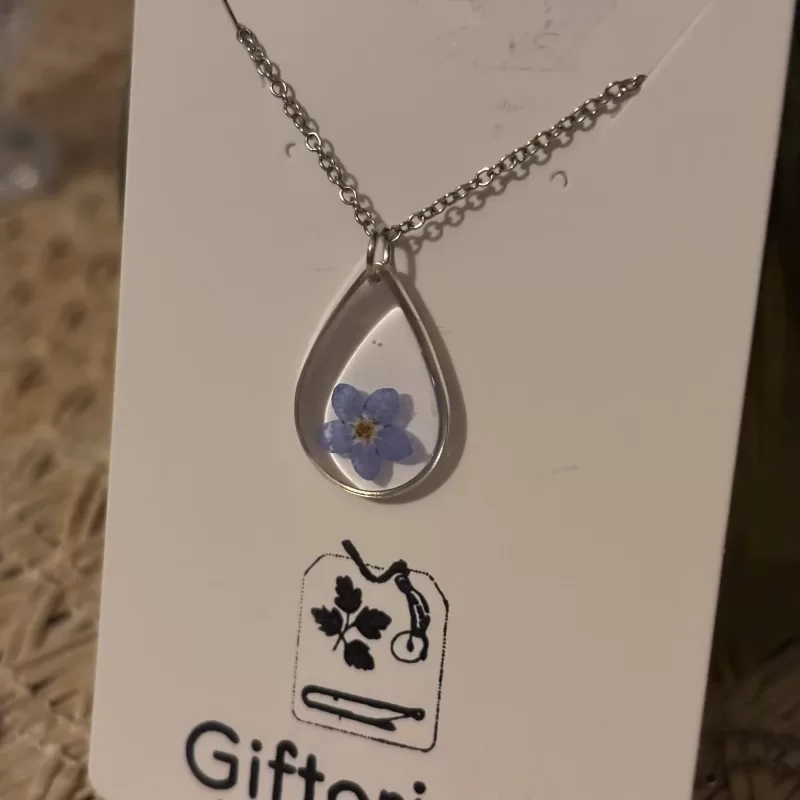 Vrouw draagt de handgemaakte RVS ketting met een hanger met daarin een echt vergeet-mij-nietje.