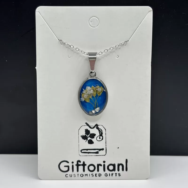 Handgemaakte blauwe droogbloemen ketting met ovale zilverkleurige hanger en witte bloemetjes op Giftorianl kaart.