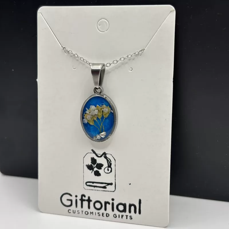 Close‑up van ovale zilverkleurige hanger met witte droogbloemen op blauwe achtergrond