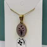 Close‑up van ovale goudkleurige hanger met rood tulpdesign op licht gemarmerde achtergrond.