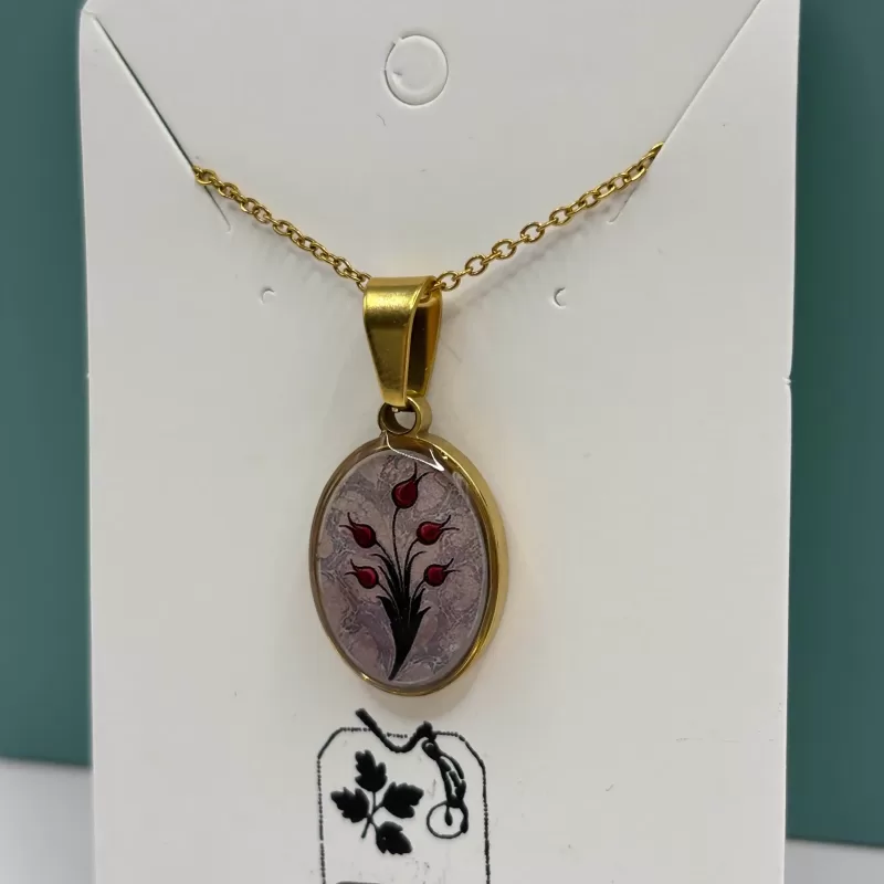 Close‑up van ovale goudkleurige hanger met rood tulpdesign op licht gemarmerde achtergrond.