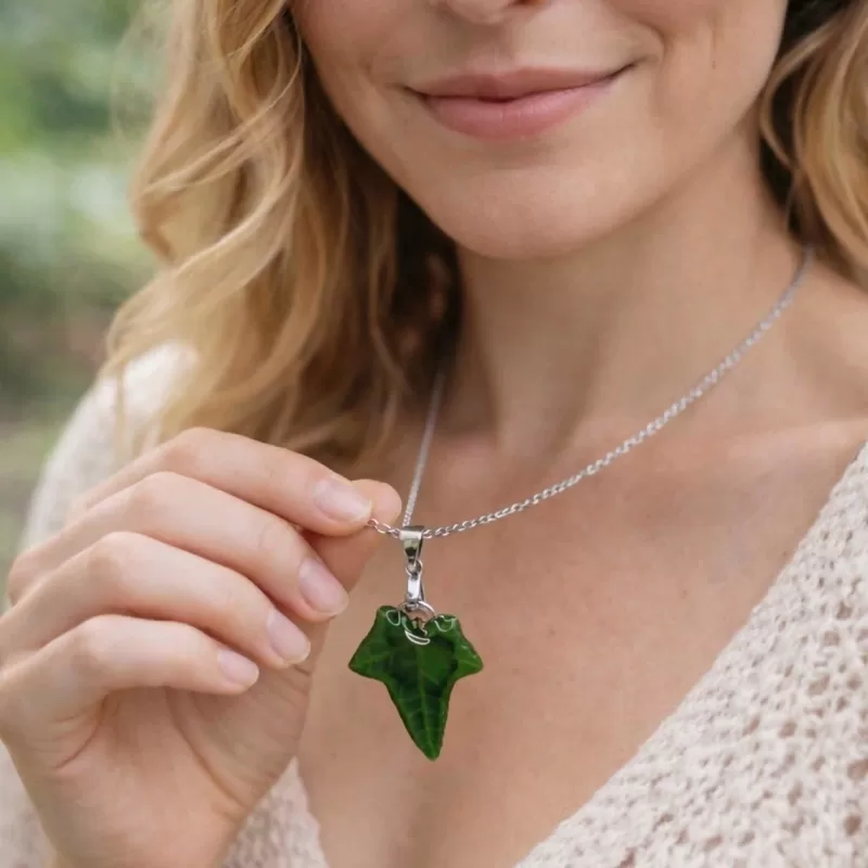 Verjaardagscadeau ketting met groene bladhanger aan zilverkleurige ketting in de hand van een vrouw.